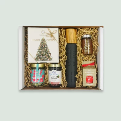 A gift box containing a bottle of Greek olive oil, a Christmas-themed box of chocolates, a jar of mountain tea, a jar of Kalamata olives, a jar of mandarin marmalade, and a jar of Greek honey with cinnamon and raisins. The items are nestled in wood wool within a cardboard box.