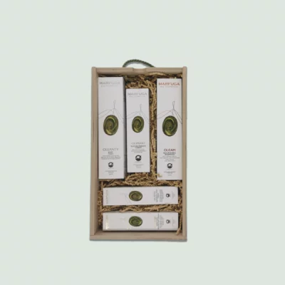 A wooden gift box containing various Marfuga Bio Cosmetics skincare products. The products are arranged neatly in wood wool and include body wash, nourishing oil, shampoo, hand and face cream. The box has a green rope handle.