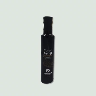 A black bottle of Mellona Carob Syrup with a black cap and label, displaying the product name in English and Greek, and a small logo at the bottom.