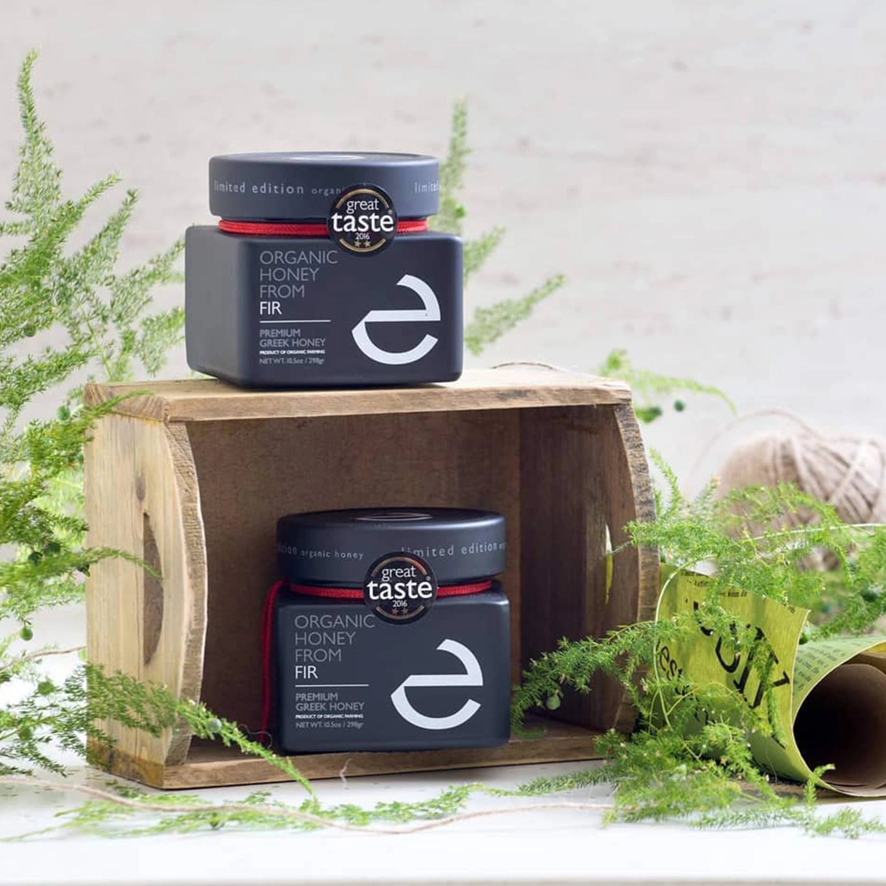 Two bottles of Eulogia’s Premium Organic Fir Honey surrounded by lush greenery, showcasing the product’s natural origin