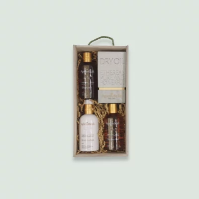 A wooden gift box containing Apiceuticals hair and skincare products. The box includes shampoo, body lotion, shower gel, and a bar of dry oil soap. The products are arranged in wood wool for an elegant presentation.