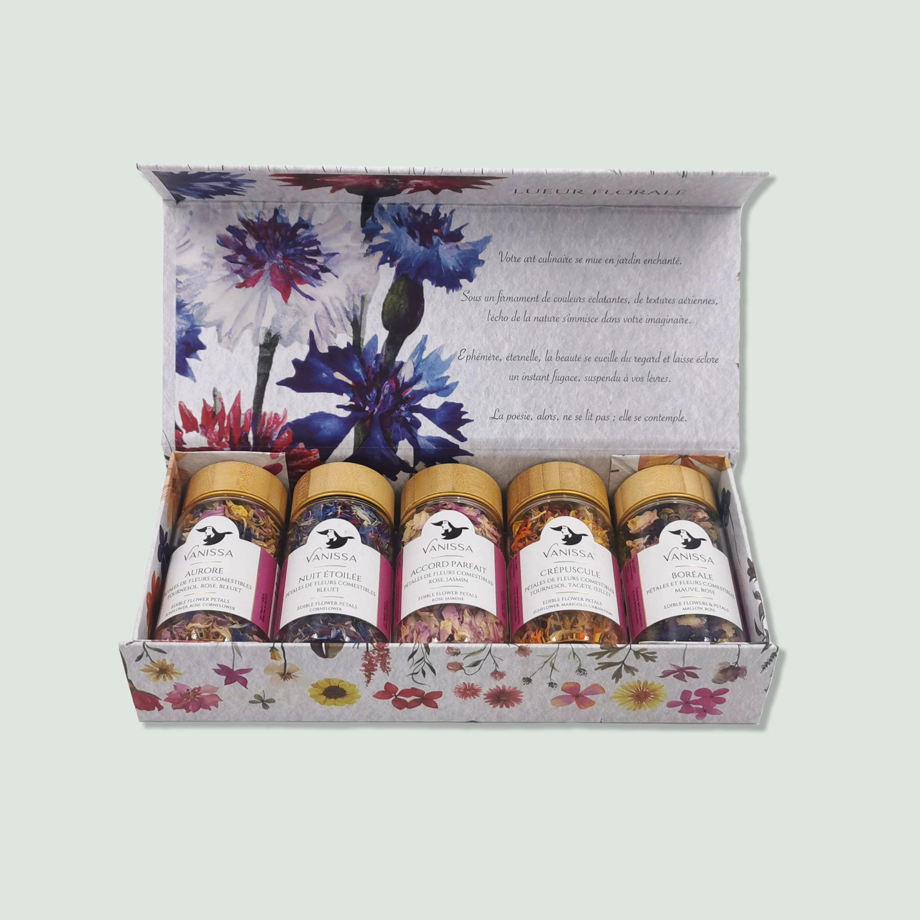 A box containing five jars of mixed herbs by Vanissa, labeled "Lueur Florale." The jars have golden lids and contain colorful blends of edible flowers and herbs. The box features a floral design with various flowers illustrated on it, and the interior lid has a poetic French text and floral imagery.