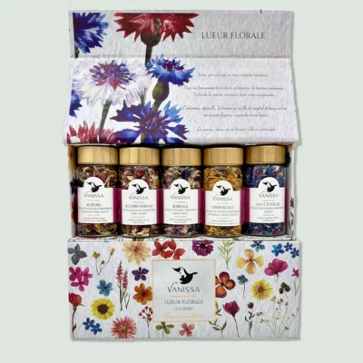 A box labeled "Lueur Florale" containing five jars of mixed herbs by Vanissa. The jars have golden lids and contain colorful blends of edible flowers and herbs. The box features a floral design with various flowers illustrated on it.