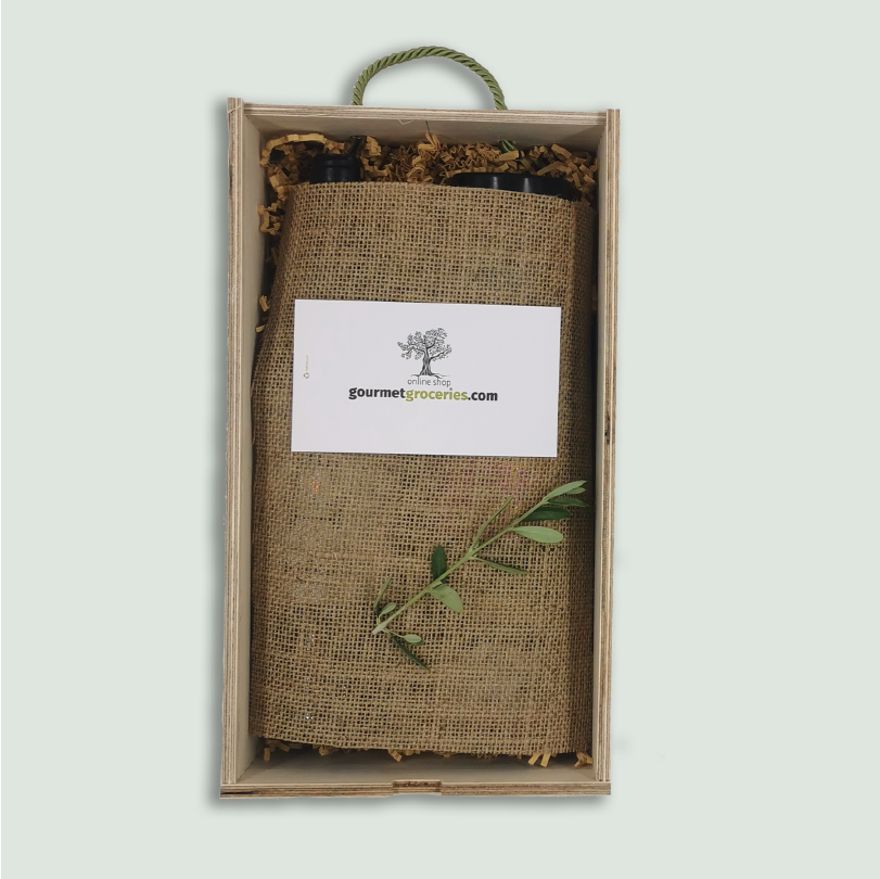 The inside of a Gourmet Groceries gift box, with products under a linen wrapping, a card, and an olive leaf.